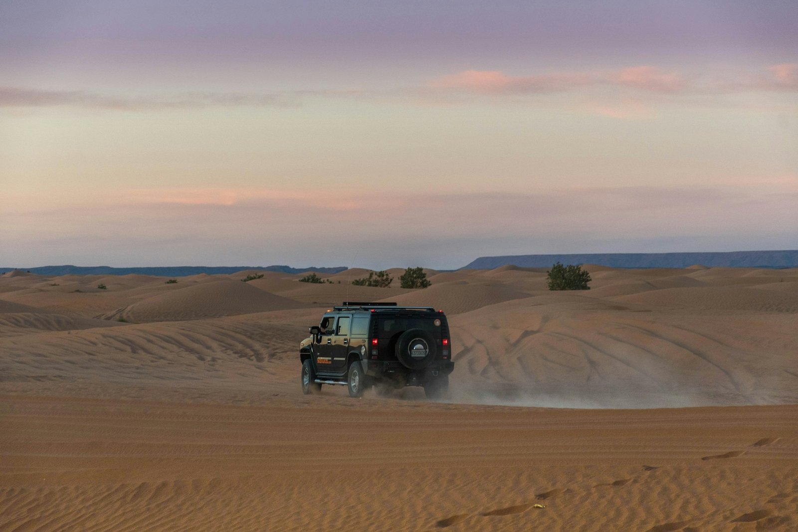 White 4x4 SUV driving across golden sand dunes in the Erg Chebbi desert near Merzouga, Morocco