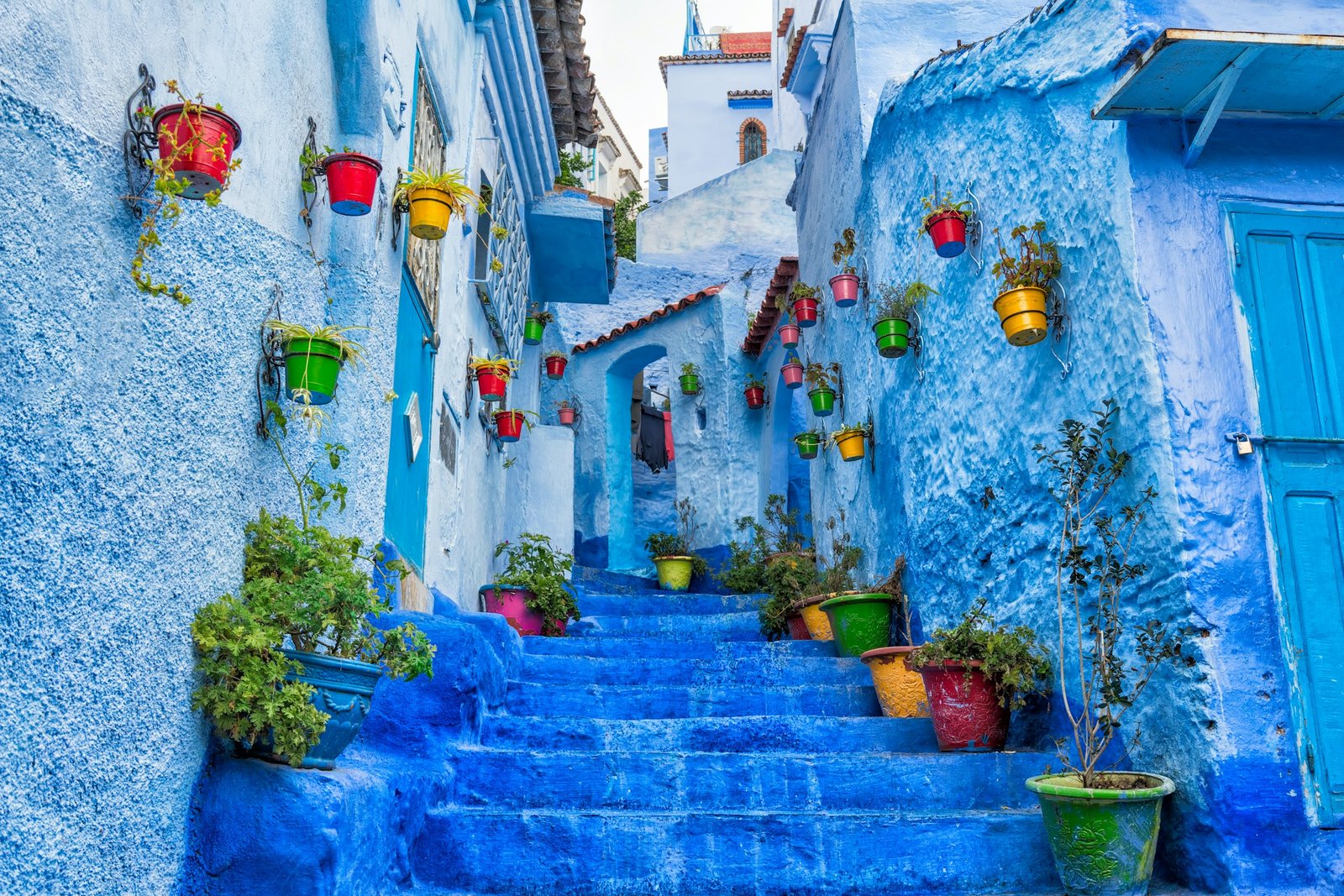 Narrow blue-painted street with steps and potted plants on Rue Bin Souaki, Chefchaouen, Morocco