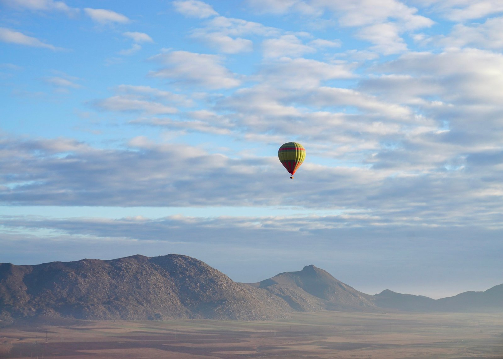 A hot air balloon drifting over the desert terrain near Marrakech, Morocco with the Atlas Mountains in the background