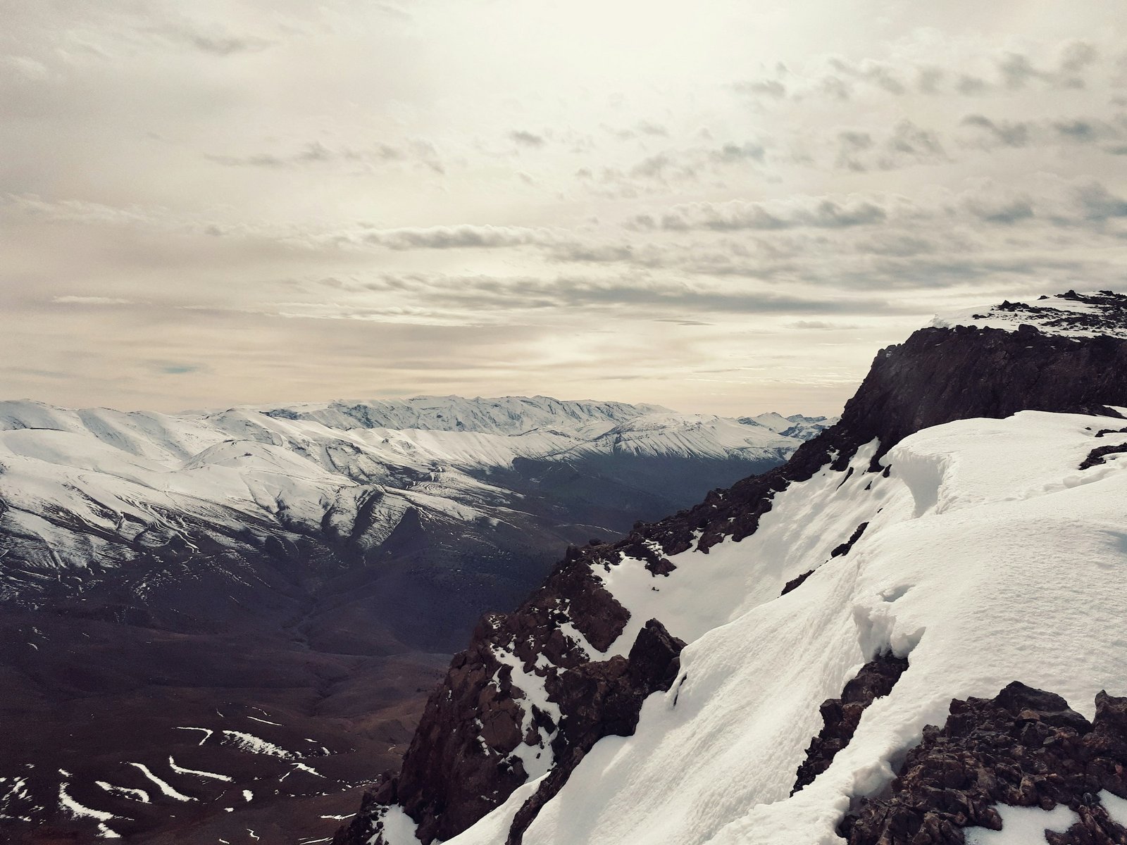 A snowboarder stands at the summit of Azourki (3,677m) in Morocco's Atlas Mountains, looking out over a snow-covered ridge