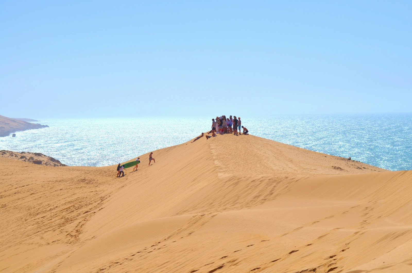 People standing with sandboards on a coastal sand dune in Imsouane, Morocco