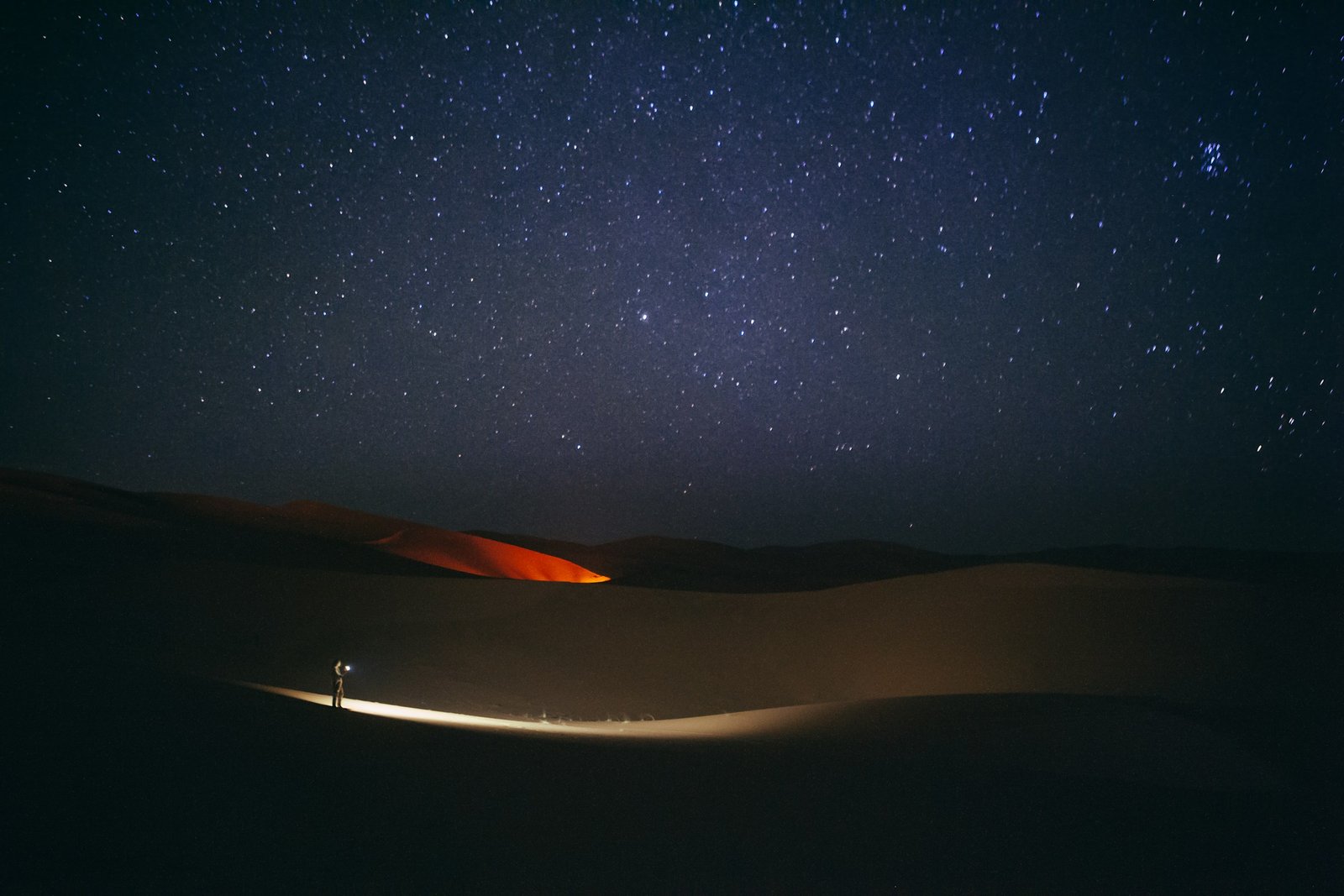 A solitary figure standing under a star-filled night sky in the Merzouga desert, Morocco